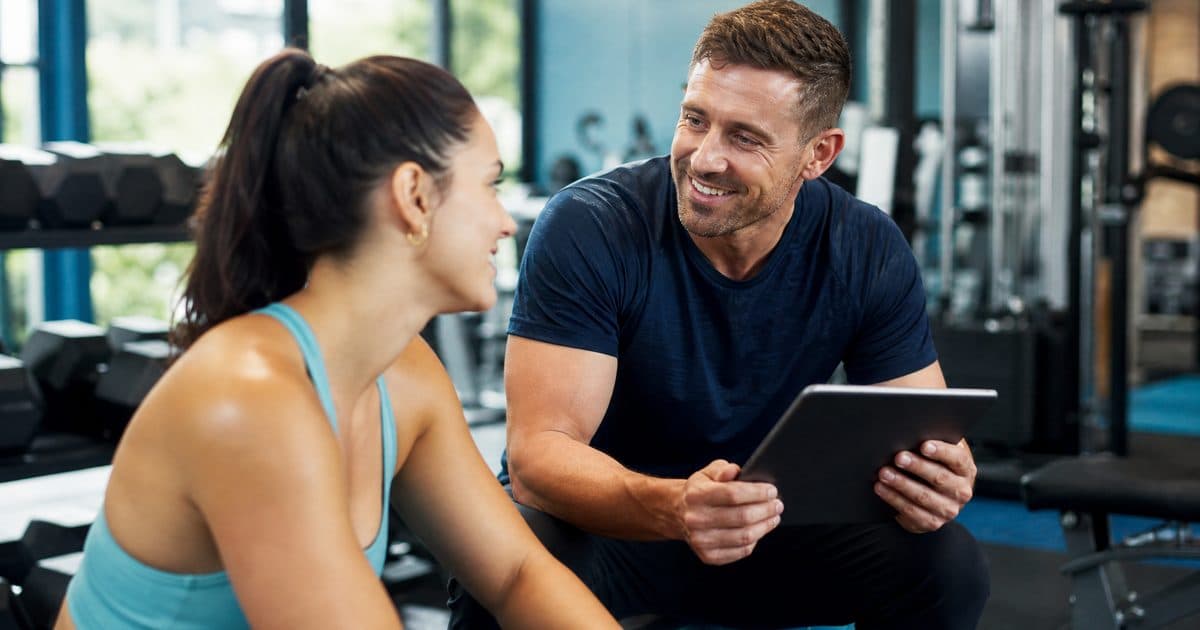 Personal trainer coaching a client and tracking progress on a tablet in a gym