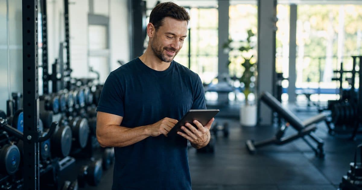 Gym owner reviewing management software on a tablet on the gym floor