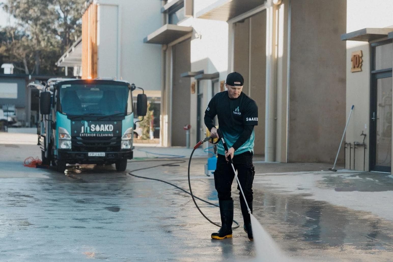 SOAKD Exterior Cleaning technician pressure-cleaning a commercial site beside a branded SOAKD truck in coastal NSW